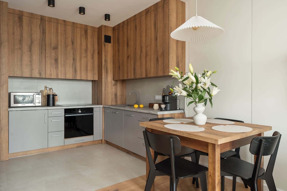 Modern kitchenette with wooden cabinets, built-in appliances, and a dining table for four, creating a cozy and functional cooking space.