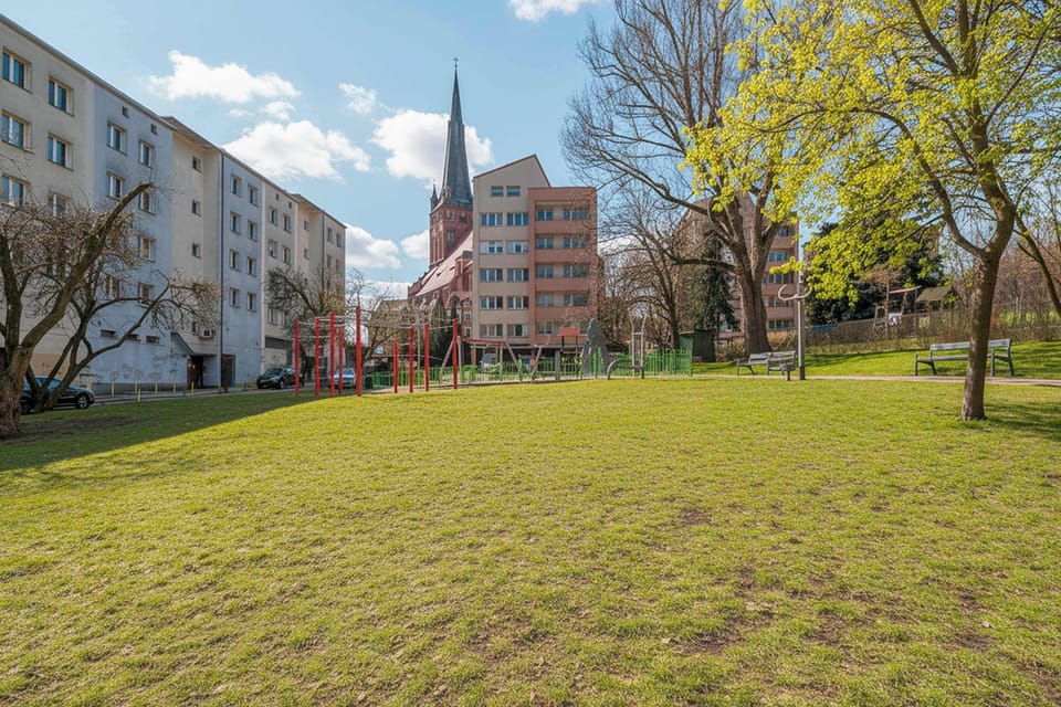 A wide grassy area near residential buildings with trees in bloom. It looks like a pleasant outdoor space for walks or relaxation.