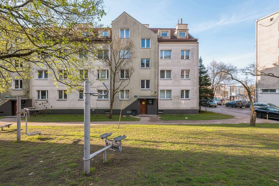 An exterior view of a residential apartment building surrounded by grass and trees. The area looks quiet and well maintained.