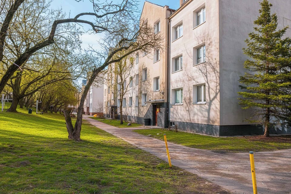 A pathway running between apartment buildings with greenery on both sides. The setting feels peaceful and residential.