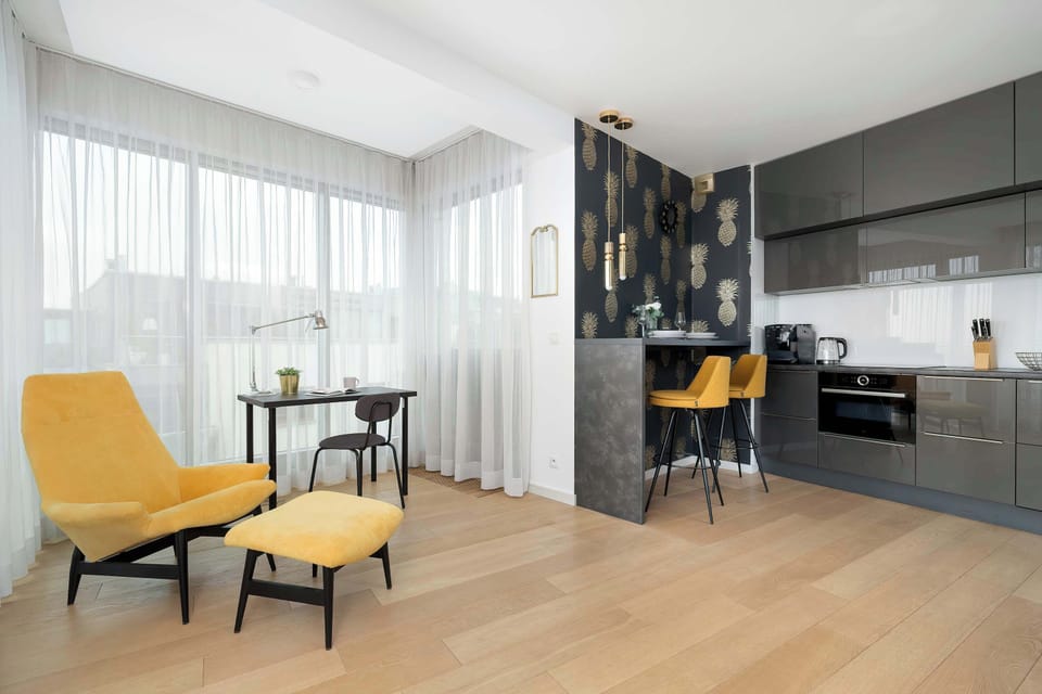 A bright living room with a comfortable armchair and footrest, complemented by a small desk by the window, creating a functional area for work and relaxation.