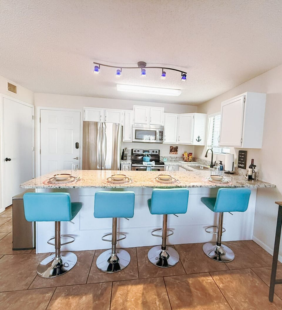 Modern coastal kitchen with granite countertops, stainless steel appliances, and stylish turquoise bar stools perfect for entertaining.