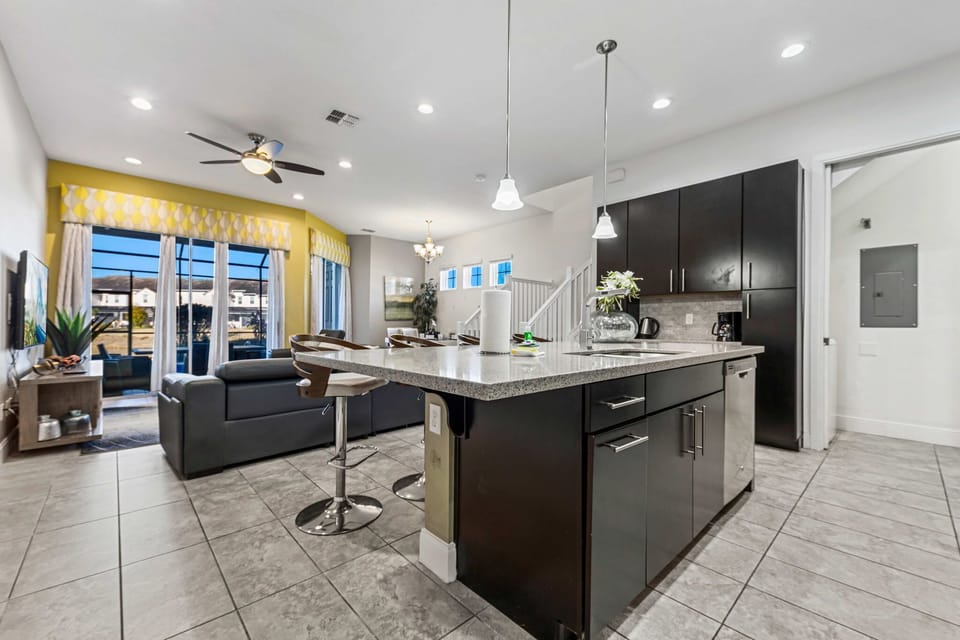 Modern kitchen island with bar seating opens to a bright living area with large windows.