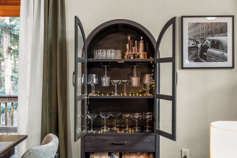 🍸✨ Cheers corner! A charming built-in bar cabinet stocked with glassware and warm twinkle lights—perfect for mixing cocktails and winding down after a day of adventure.