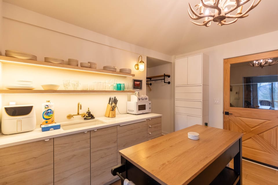 Warm, well-stocked kitchen at Moondrift Retreat with glowing open shelves and a rustic antler chandelier overhead.