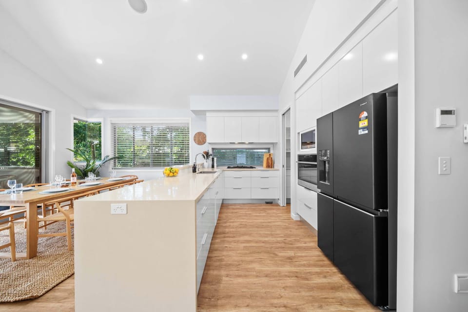 A modern kitchen with a large island bench, butlers pantry and sleek black fridge.