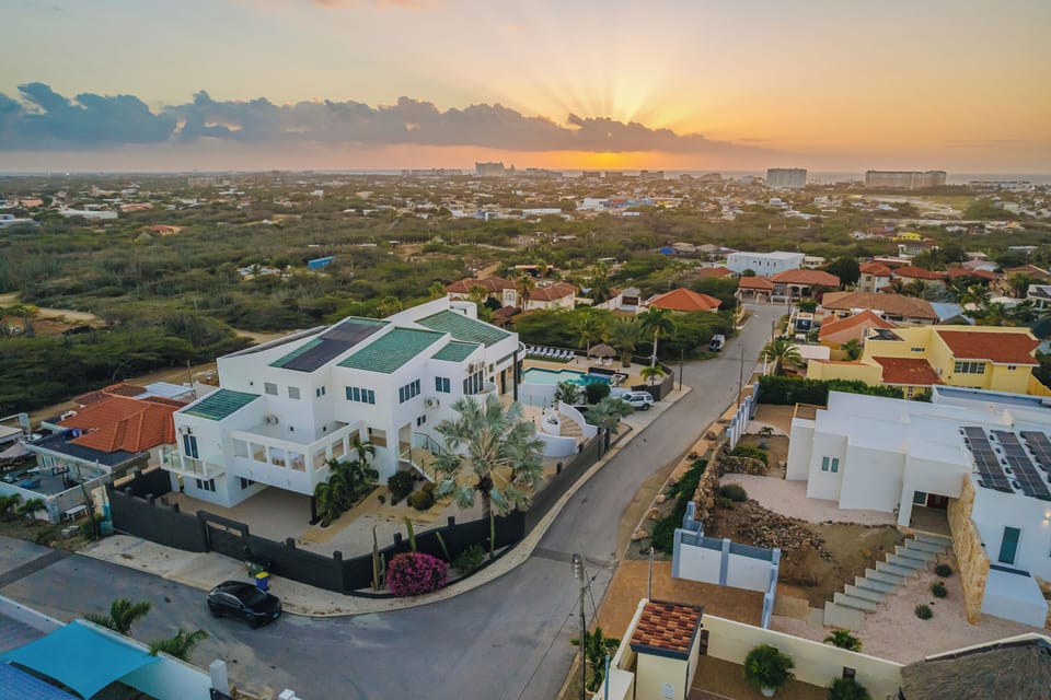Golden hour from above: a breathtaking drone view from the hilltop villa stretching across Aruba’s coastline toward the High Rise skyline, where the Ritz-Carlton and Marriott glow as the sun melts into the Caribbean Sea.
