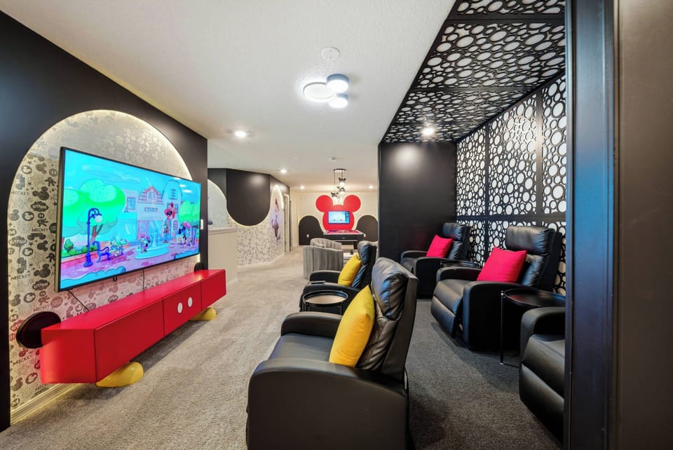 Enjoy a stylish movie night in plush black leather recliners with a vibrant red accent wall and playful decor that set a fun atmosphere. Relax and unwind as you watch your favorite shows on the large screen.