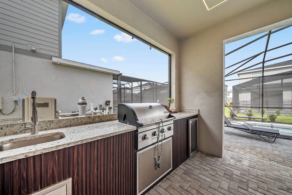 Discover a stylish outdoor kitchen with rich wooden cabinetry and sleek granite countertops, ideal for grilling and entertaining. Expansive windows invite natural light, creating a bright and seamless indoor-outdoor atmosphere.