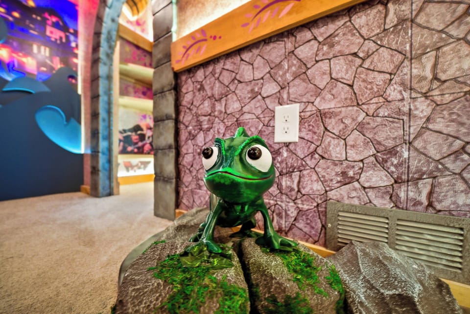 A whimsical touch awaits you with a charming chameleon statue perched on a textured stone-like base, set against a playful backdrop of vibrant colors. The unique decor invites a sense of wonder, making every corner an adventure.