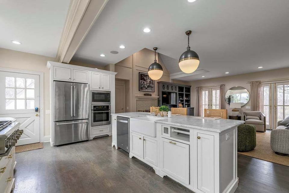 The open-plan keeping room flows straight into the
kitchen — green velvet ottomans double as a coffee table, and the island is just behind you.
One continuous gathering space.