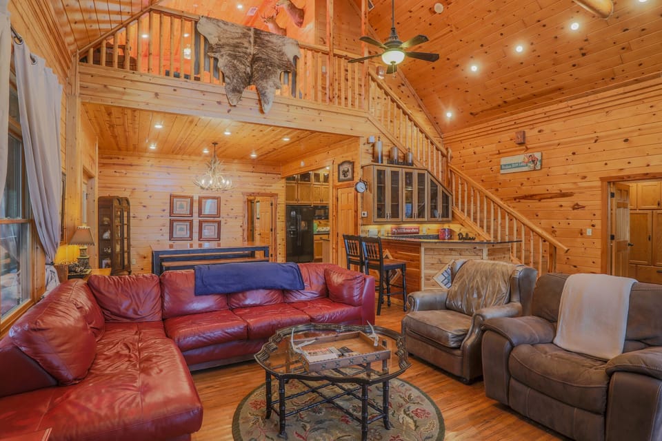 Open-concept living — leather sofas, antler chandelier, wood-paneled warmth