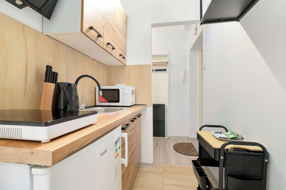 Another angle of the kitchen showing appliances, storage, and a small dining stool. The layout is practical and well-organized. The kitchen connects seamlessly with the rest of the apartment.