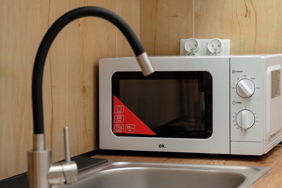 A close-up of the sink area with a modern black faucet and a microwave placed above the counter. The image highlights the apartment’s practical amenities.