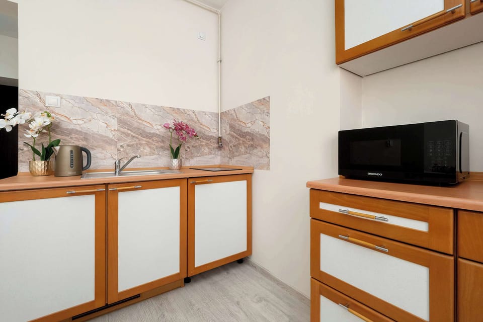 A kitchen countertop view with wooden cabinetry, a microwave, kettle, and backsplash with a marble-style pattern.