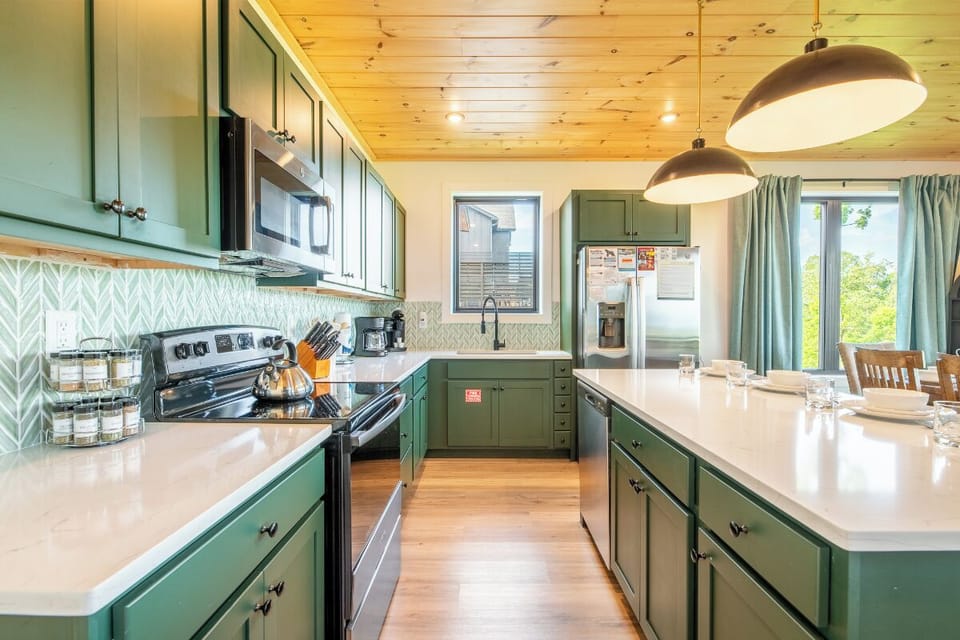 This spacious kitchen blends rustic charm with modern convenience, featuring green cabinetry, gleaming countertops, and full-sized appliances—everything you need to whip up meals with ease during your stay.