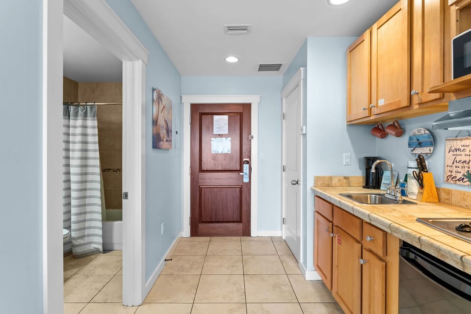 Your spacious open-plan suite combines kitchen convenience with coastal comfort, featuring warm wood cabinetry and soothing blue walls for your perfect beach getaway.