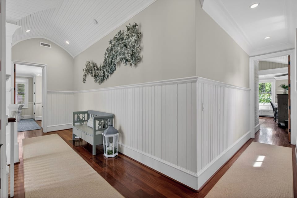 Your charming upstairs hallway features beautiful beadboard wainscoting, gleaming hardwood floors, and vaulted ceilings that create an airy, coastal cottage feel.