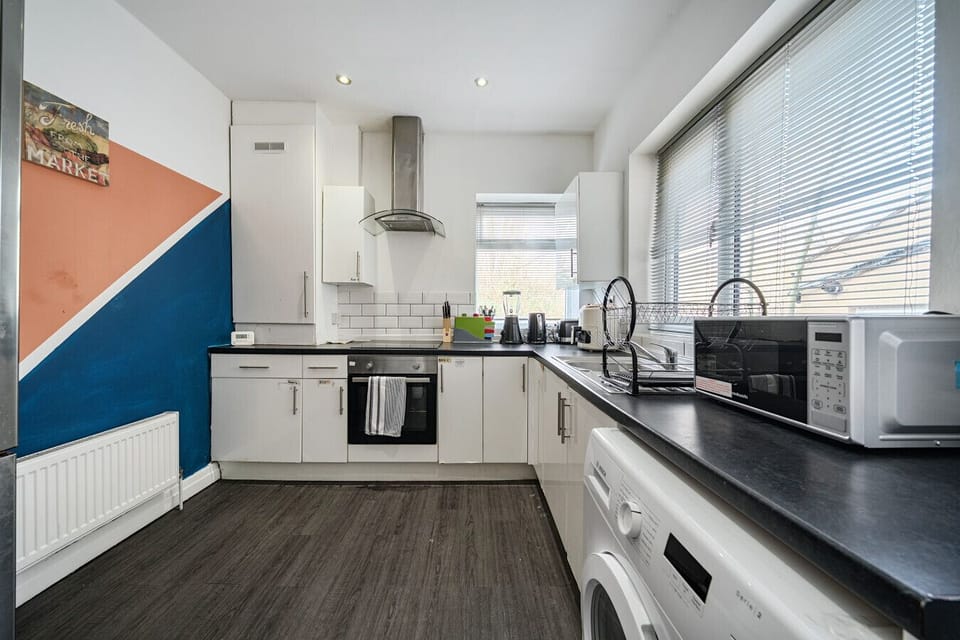 A practical space for preparing group meals, with white fitted units, an integrated oven, hob, extractor hood, microwave and washing machine.