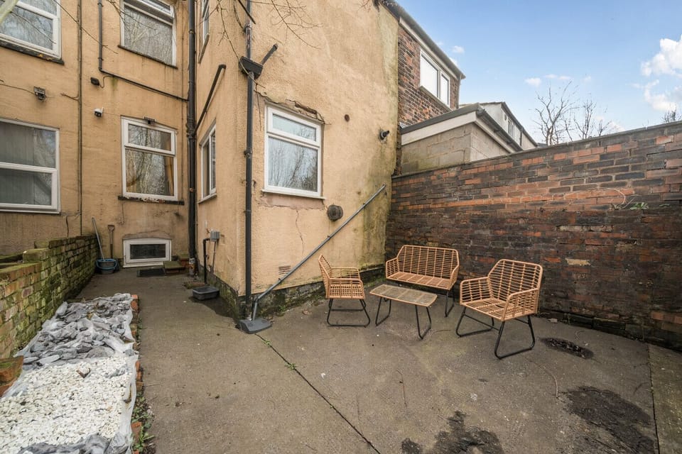 Rear yard with a concrete floor, rattan garden chairs and a low table set against brick walls.
