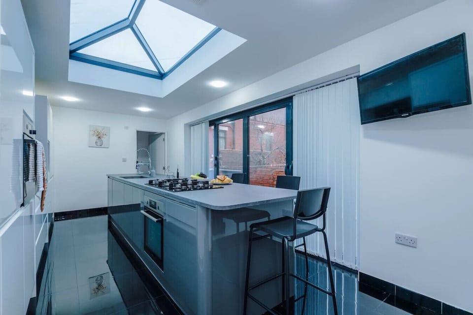 Wide kitchen view showing the island, skylight, glossy floor, and a wall-mounted TV.