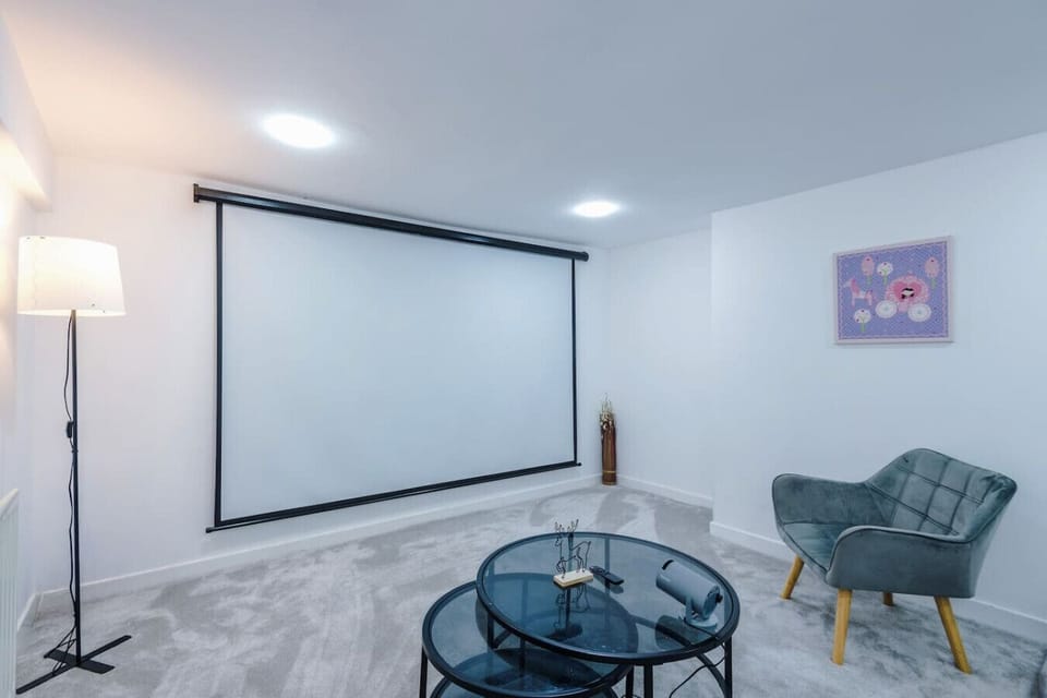 Cinema room with a large wall-mounted projector screen, floor lamp, glass coffee table, and an upholstered chair.