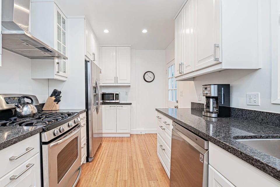 A bright, white kitchen showcases stainless steel appliances and clean finishes, blending style with everyday functionality
                