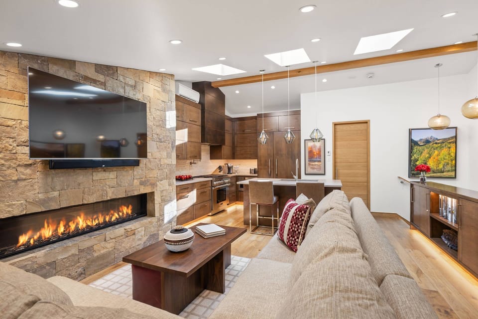 A dramatic stacked-stone fireplace anchors this sunlit living space, seamlessly connected to the gourmet kitchen.