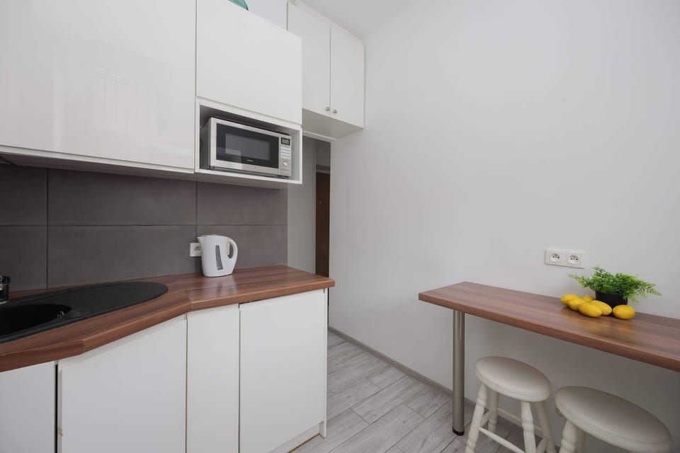 The compact kitchen includes white lower cabinets and a small breakfast bar with two stools. A bowl of lemons on the wooden counter adds a bright splash of color to the white interior.