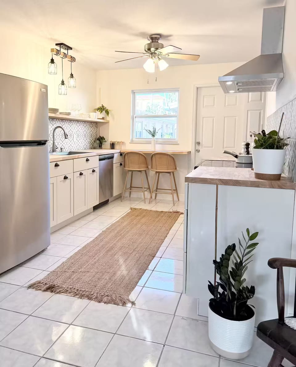 Cook homemade meals in this bright, modern, and well‑stocked kitchen featuring stainless‑steel appliances, warm butcher‑block counters, a custom tile backsplash, fresh greenery accents, and a charming breakfast nook overlooking the backyard.