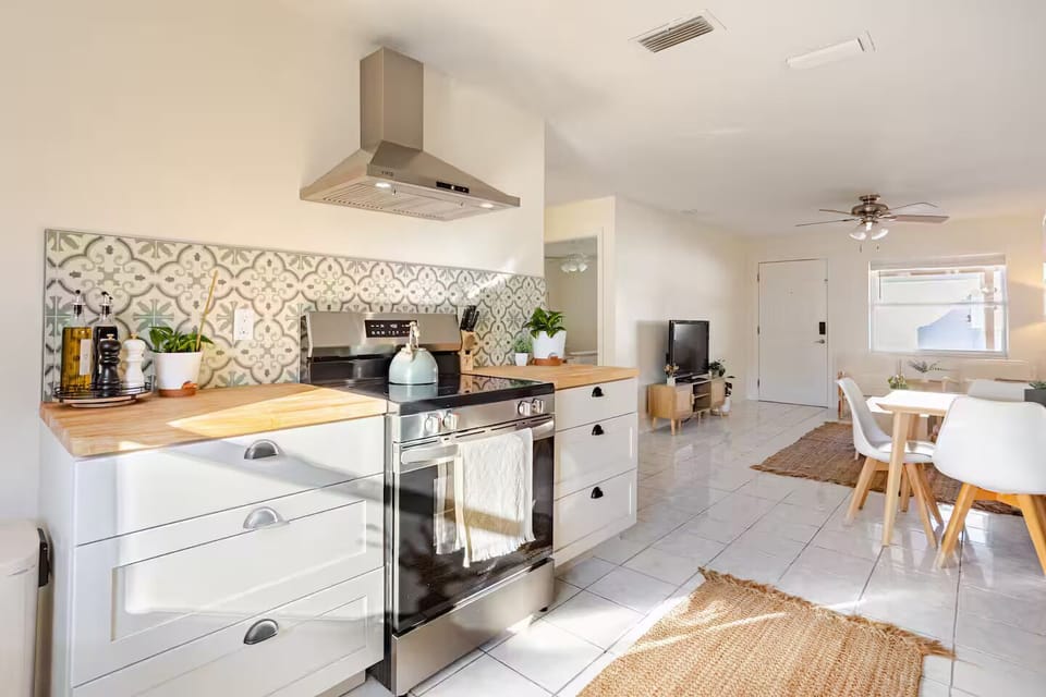 Cook homemade meals in this bright, modern, and well‑stocked kitchen featuring stainless‑steel appliances, warm butcher‑block counters, a custom tile backsplash, fresh greenery accents, and a charming breakfast nook overlooking the backyard.
