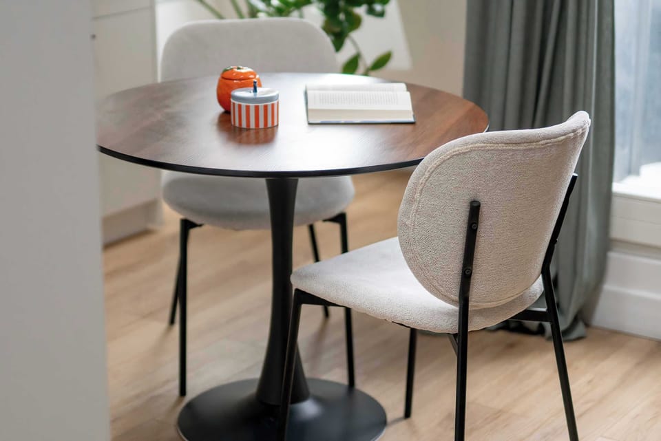 The dining area is furnished with a round dark table and two elegant grey chairs. Subtle decor on the table adds a touch of sophistication to this functional corner.