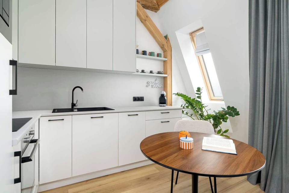 A compact, fully equipped kitchen features white cabinets and a dark countertop. A small wooden dining table serves as a central point for meals or morning coffee.