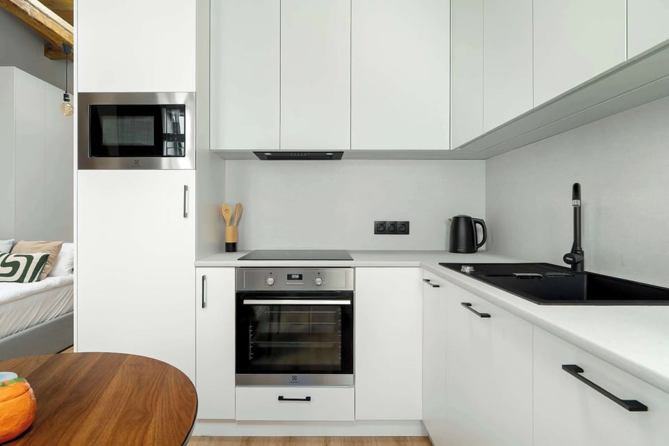 The kitchen workspace shows an oven, induction hob, and integrated microwave. The clean, monochromatic design is complemented by high-quality appliances for home cooking.