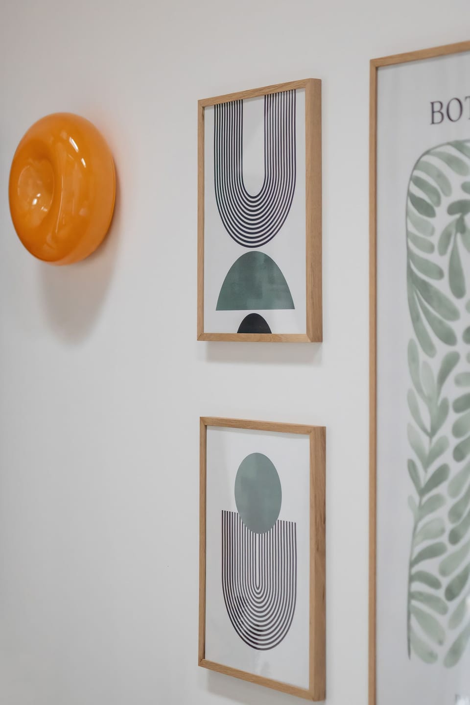 Minimalist wall decor consists of two framed abstract prints and a round orange accent piece. The white walls and clean lines emphasize the contemporary aesthetic of the interior.