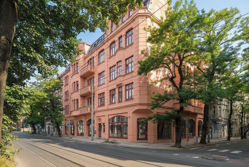 The exterior view shows a beautifully restored, building surrounded by lush green trees. Its classic architecture stands out, suggesting a prestigious and charming location.