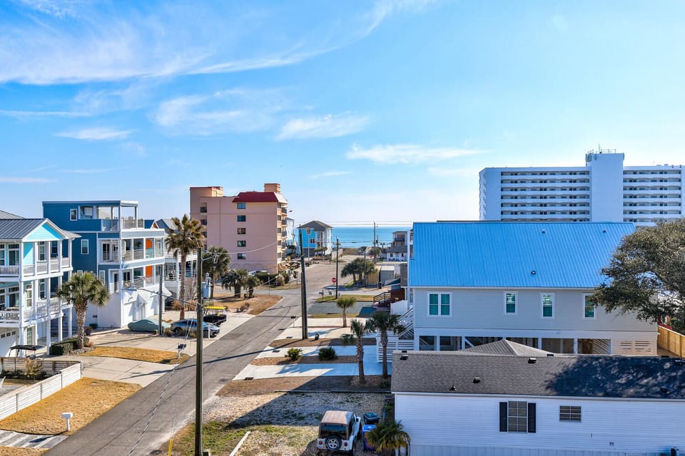 Coastal neighborhood with beach access featuring diverse vacation homes, high-rise hotels, and palm trees under bright blue skies.