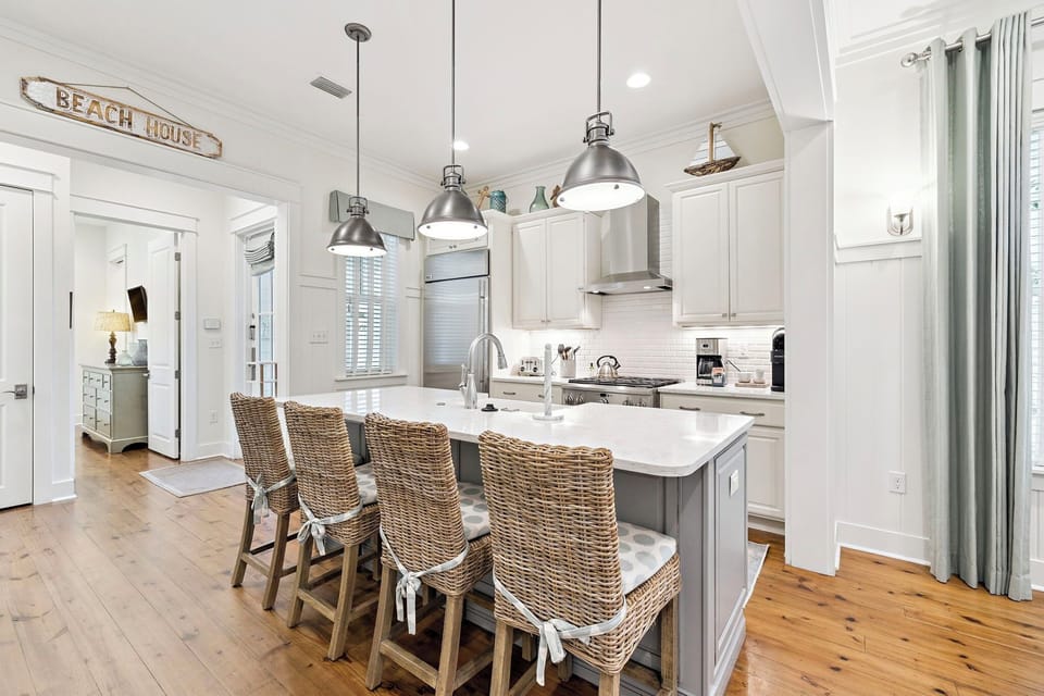 Your coastal-inspired kitchen awaits with marble countertops, pendant lighting, and wicker bar stools perfect for morning coffee or evening conversations.