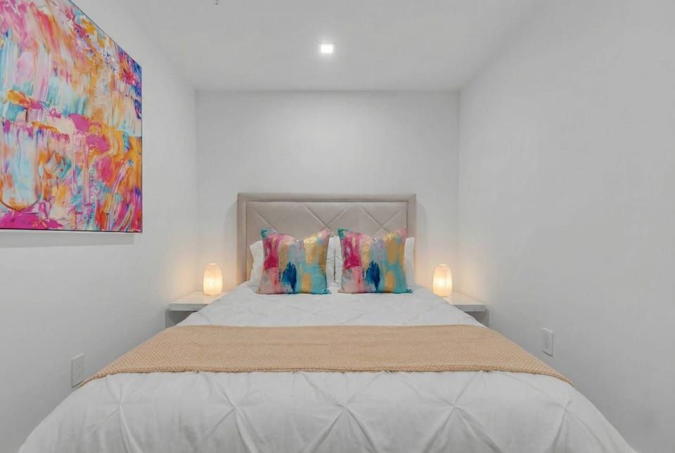 This private, windowless den features a cozy full-size bed accented by vibrant, abstract art and colorful textiles. The minimalist white space offers a peaceful, dark environment—perfect for guests seeking a deep, uninterrupted night's sleep.