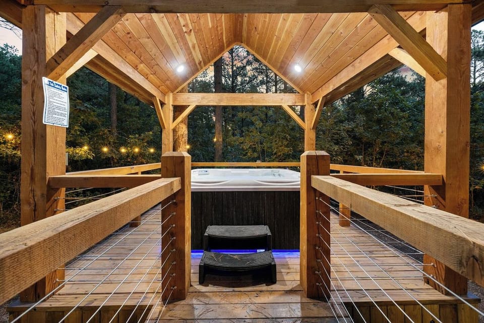 Private covered hot tub pavilion with string lights and pine tree views at Broken Bow luxury cabin