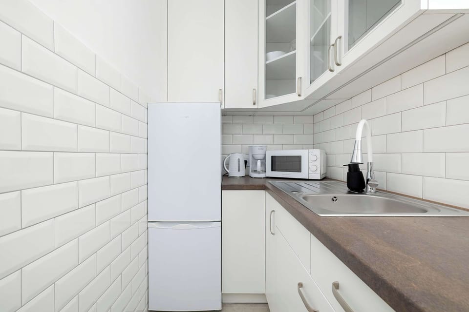 Full view of white kitchen cabinets with refrigerator, microwave, and coffee maker. The light finish contrasts with the darker countertop, creating a clean and modern look.