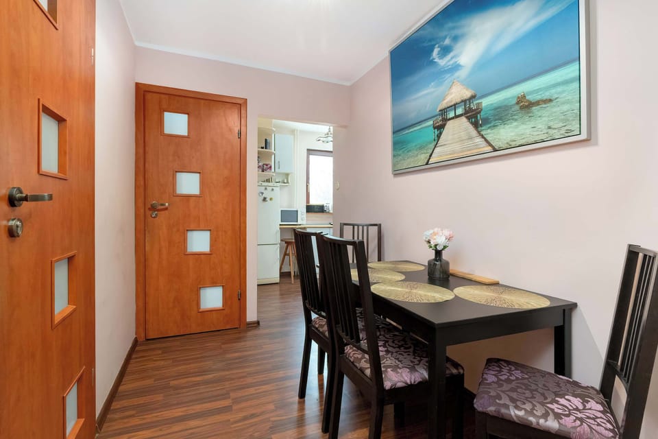 A dining area transitions smoothly into the hallway, featuring a dark wooden table with matching chairs. A tropical beach painting on the wall adds a splash of color to the neutral interior.
