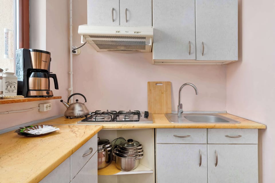 A close-up of the kitchen shows the organized workspace with a kettle, sink, and wooden cutting board. Overhead white cabinets provide ample storage for kitchen essentials.