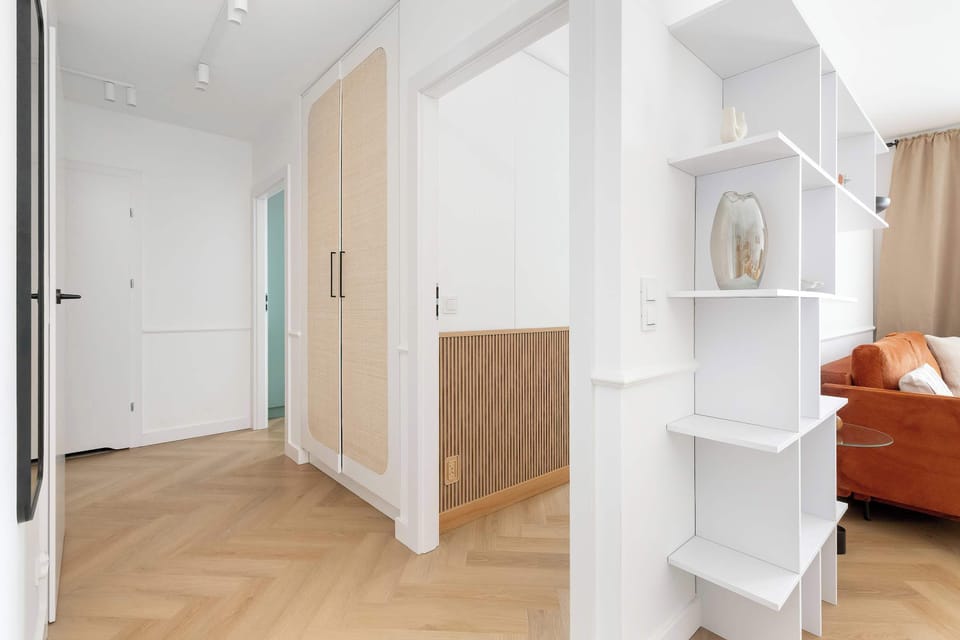 The hallway features bright wooden flooring and white built-in storage solutions. A decorative wall niche and clean lines lead the eye toward the living areas of the apartment.