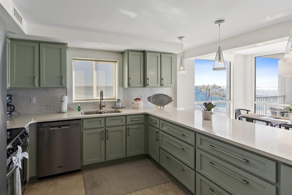 Cook with stunning ocean views from your modern kitchen featuring sage green cabinets and gleaming countertops.