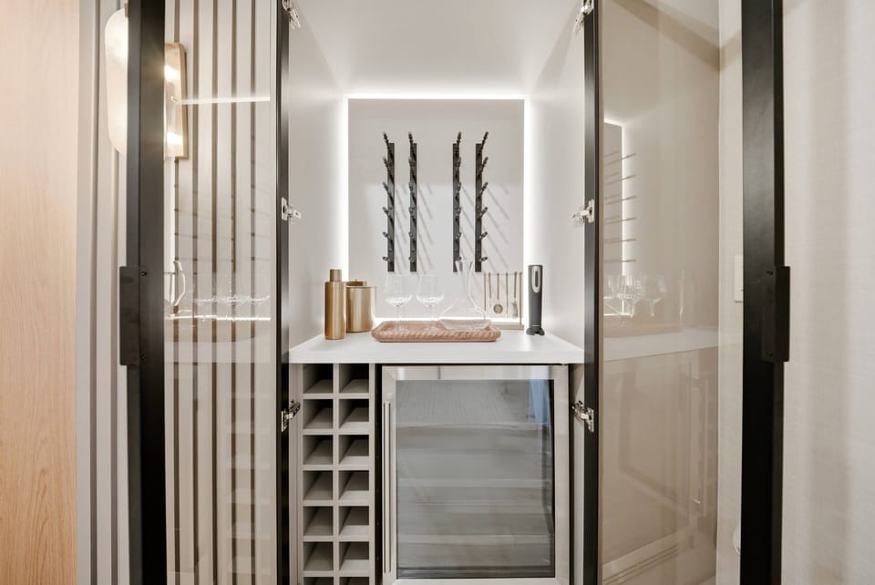 Experience our stylish bar area with a sleek wine fridge and polished countertop, ideal for gatherings. The minimalist decor, enhanced by beautiful artwork and warm lighting, offers a relaxing and inviting atmosphere just for you.