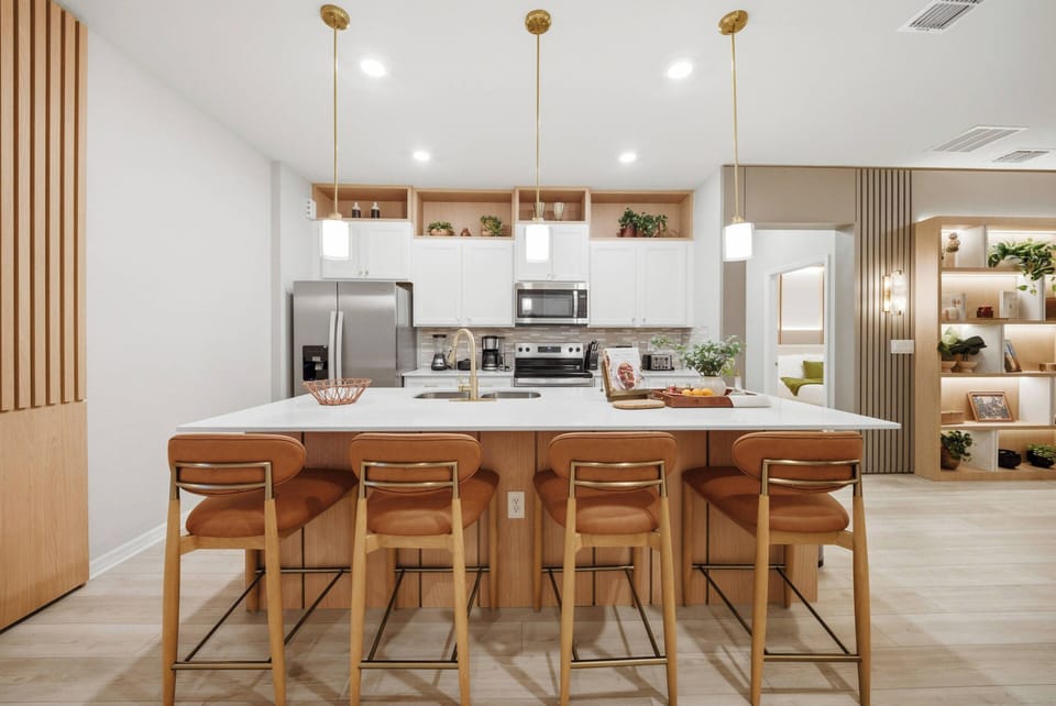 Discover the heart of the home in this stylish kitchen featuring a spacious island, warm wood accents, and modern bar stools. Bright pendant lighting highlights the open layout, creating a seamless flow to the inviting living.