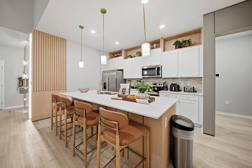 This bright kitchen features sleek white cabinetry and a spacious island perfect for morning coffee or evening gatherings, complemented by warm wood accents and modern fixtures that create an inviting atmosphere for your culinary.