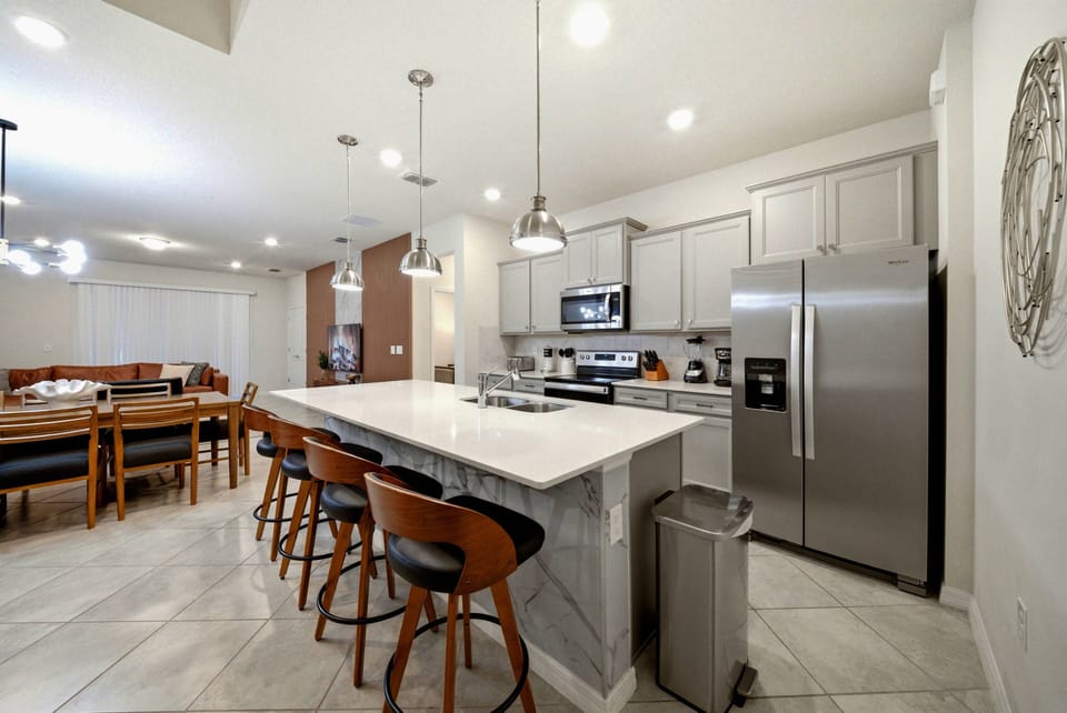Welcome to this bright kitchen, featuring sleek stainless steel appliances and crisp white cabinetry. The spacious island with stylish bar stools is perfect for casual dining or morning coffee, enhanced by charming wooden accents.