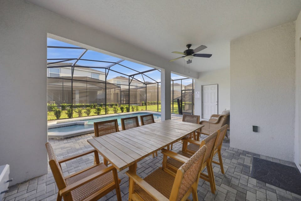 Savor meals with loved ones in our bright outdoor dining area, featuring a spacious wooden table. The screened enclosure allows for refreshing pool views and abundant natural light, elevating your indoor-outdoor living experience.